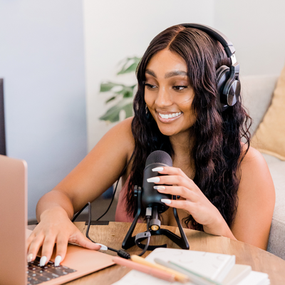 Young woman recording with a mic and laptop, smiling and wearing headphones.