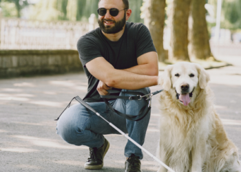 Man crouching with white cane an guide dog.