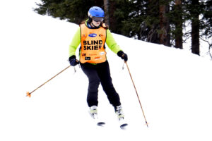 Woman skiing down a slope, with a vest that says :blind skiier: