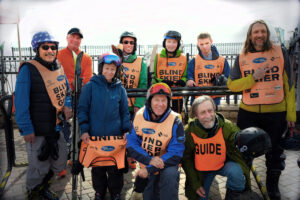 Group of people posing for a photo, all wearing orange vests and ski gear.