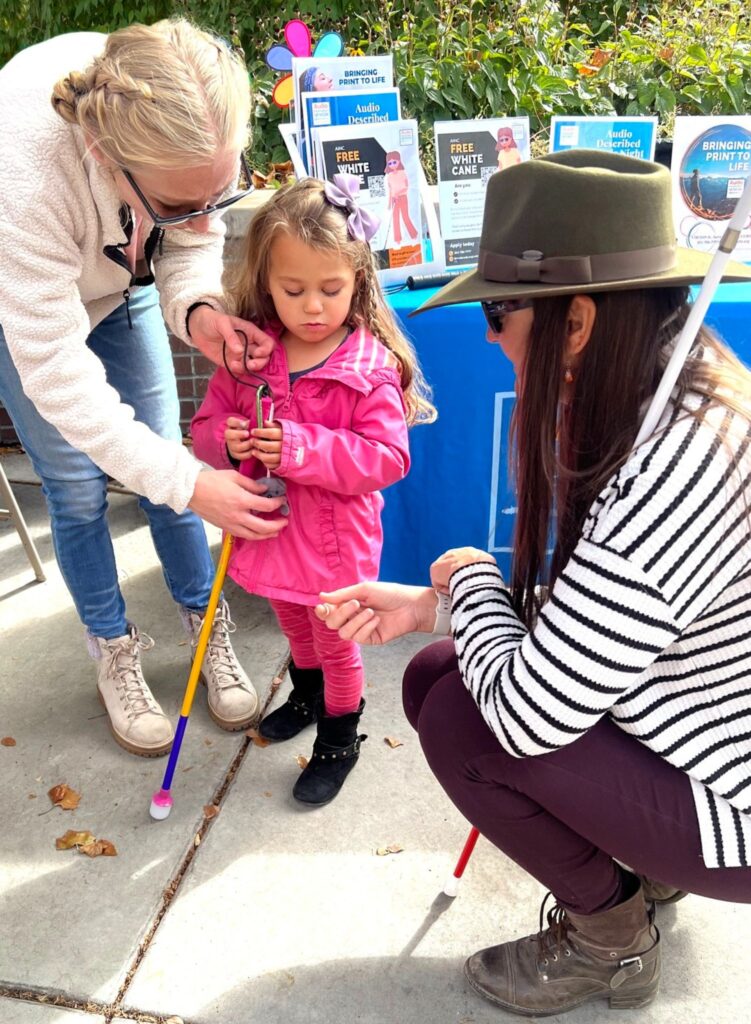 Penn Street is with a little girl and her mom talking about the white cane project.